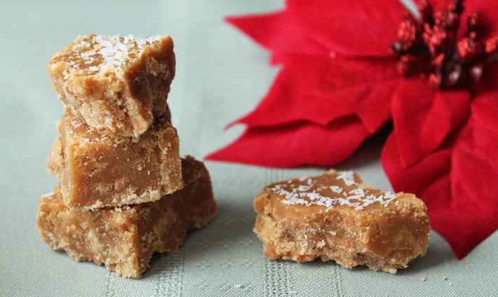 Four pieces of Vegan Coconut Fudge sitting on a green tablecloth with a Christmas flower in the background.