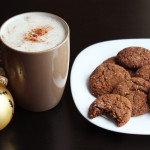 A gingerbread latte, a plate of gingerbread cookies, and a Christmas decoration on a black table.