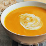 A bowl of bright orange vegan Cauliflower Sweet Potato Carrot soup in a bowl on a table.