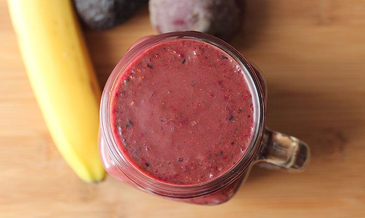Overhead shot of a Berry Beet Ginger Smoothie in a glass sitting on a wooden table.