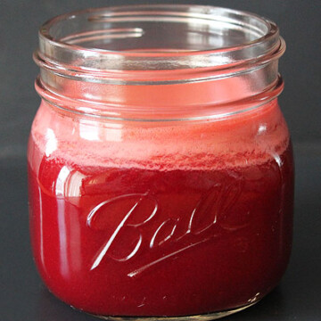 A close up of a glass jar filled with red beet carrot apple juice.