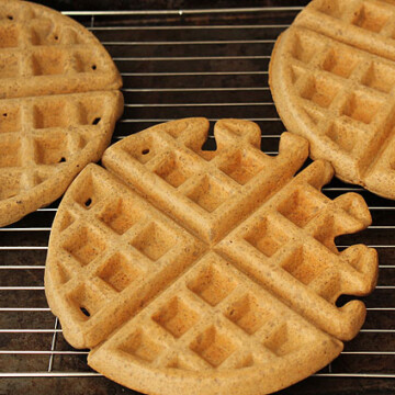Three round, freshly made waffles on a cooling rack.