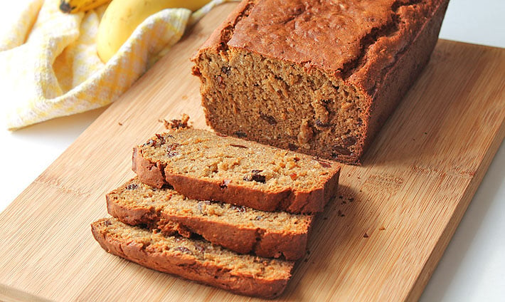 A close up of a loaf of banana bread, three pieces have been sliced and are sitting in front of the whole loaf.