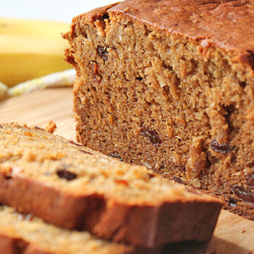 A loaf of banana bread, a few pieces have been sliced and sit in front of the loaf.