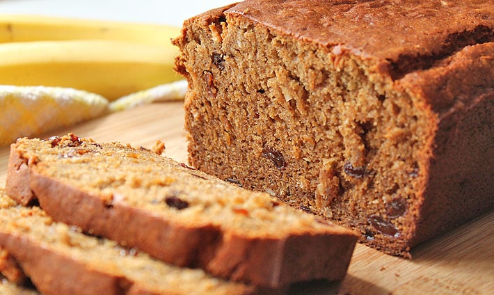 A loaf of banana bread, a few pieces have been sliced and sit in front of the loaf.