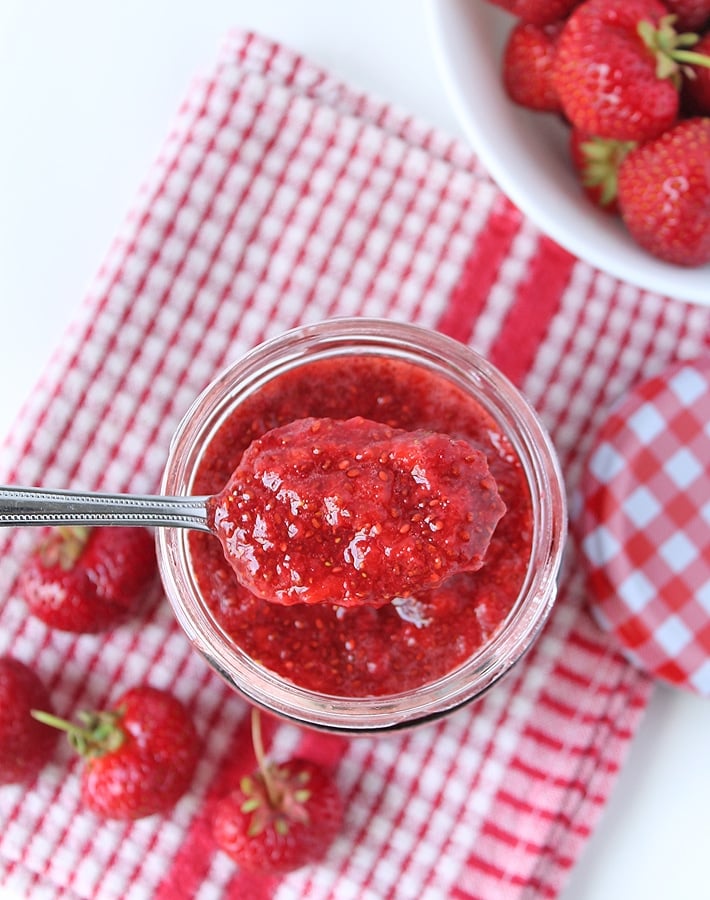 Overhead shot of Strawberry Chia Seed Jam in a spoon, the jar the jam came from is underneath the spoon.