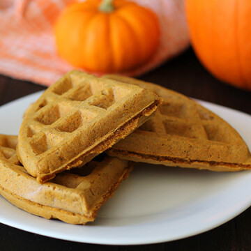 Vegan Gluten Free Pumpkin Spice Waffles on a white plate, fresh pumpkin are on the table behind the plate.