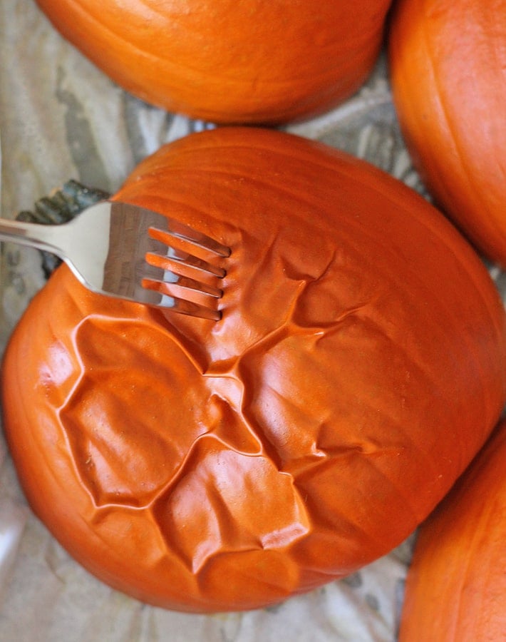 How to Make Homemade Pumpkin Puree - Cookd sugar pumpkins on a baking sheet with a fork inside of one to test doneness.