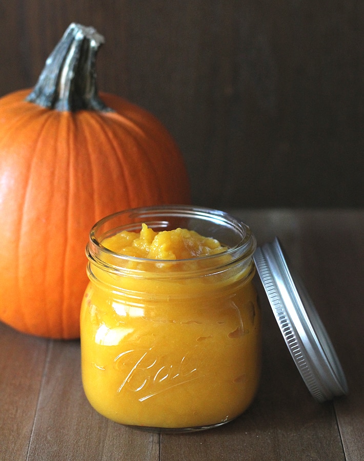 How to Make Homemade Pumpkin Puree - A sugar pumpkin and a jar of pumpkin puree on a dark table.