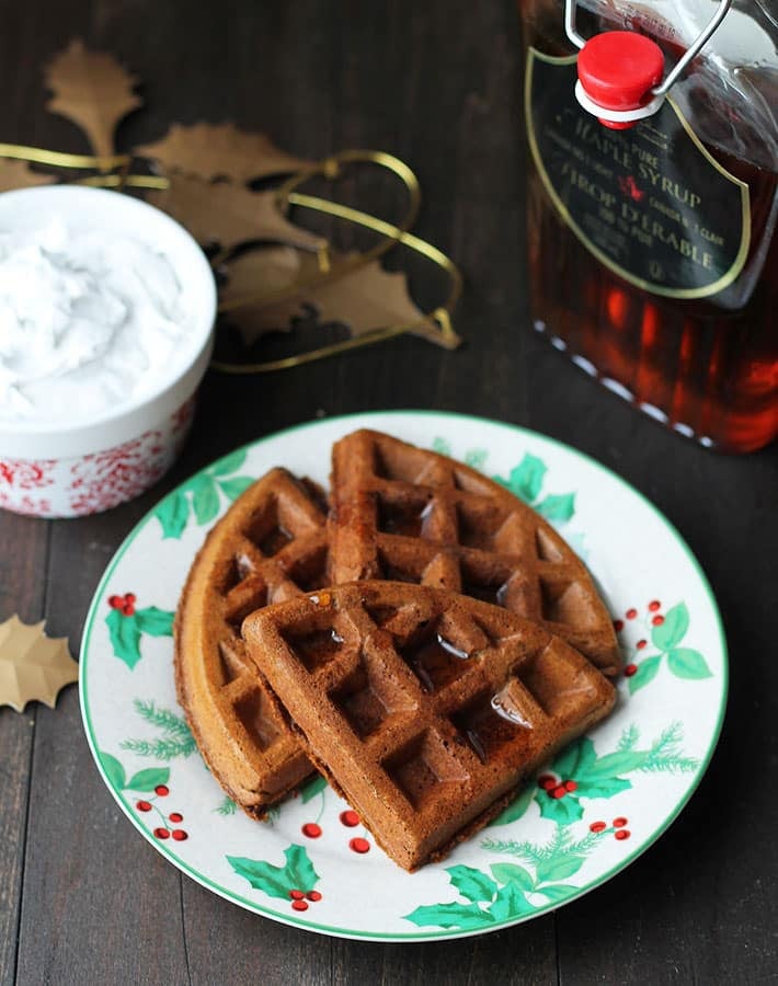 Overhead shot of Vegan Gluten Free Gingerbread Waffles on a plate with a bottle of maple syrup to the right.