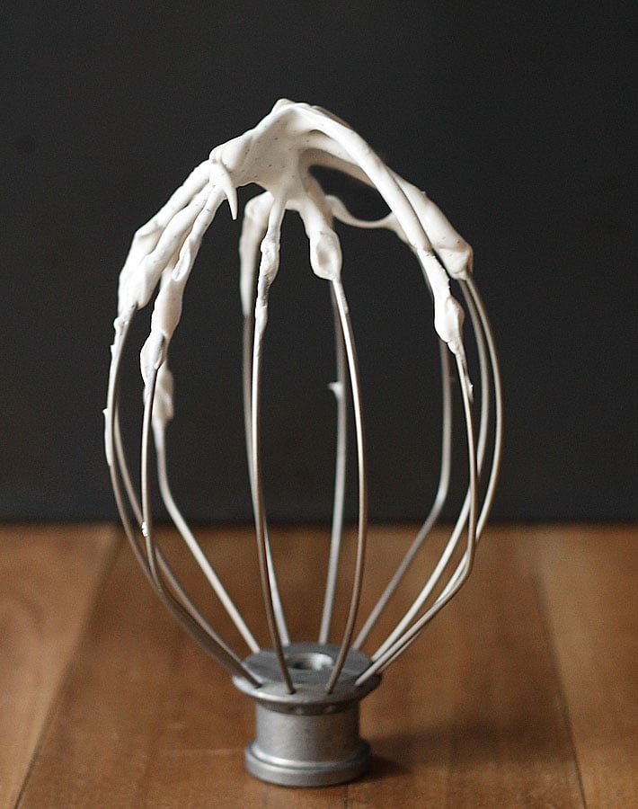 A stand mixer whisk sitting on a table with coconut whipped cream in it.