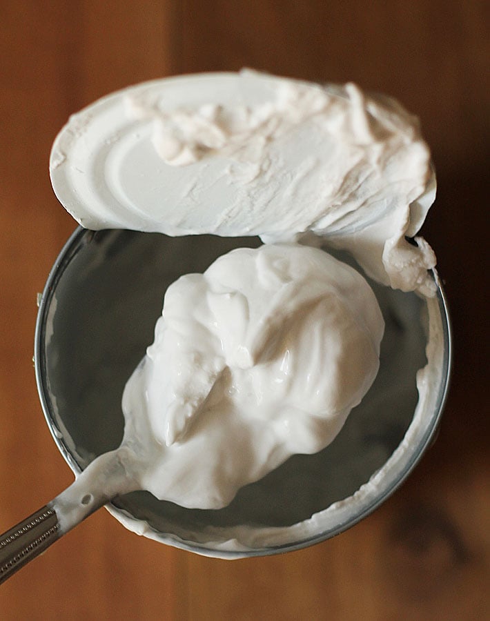 The cream from a can of coconut milk on a spoon being held over the can.