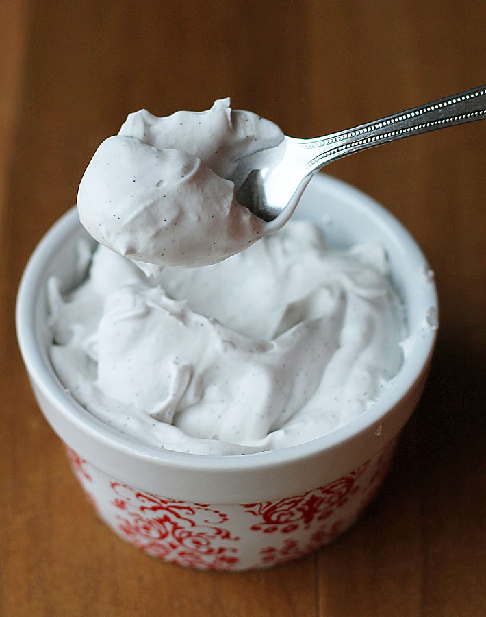 Homemade coconut whipped cream being spooned out of a small ceramic dish.