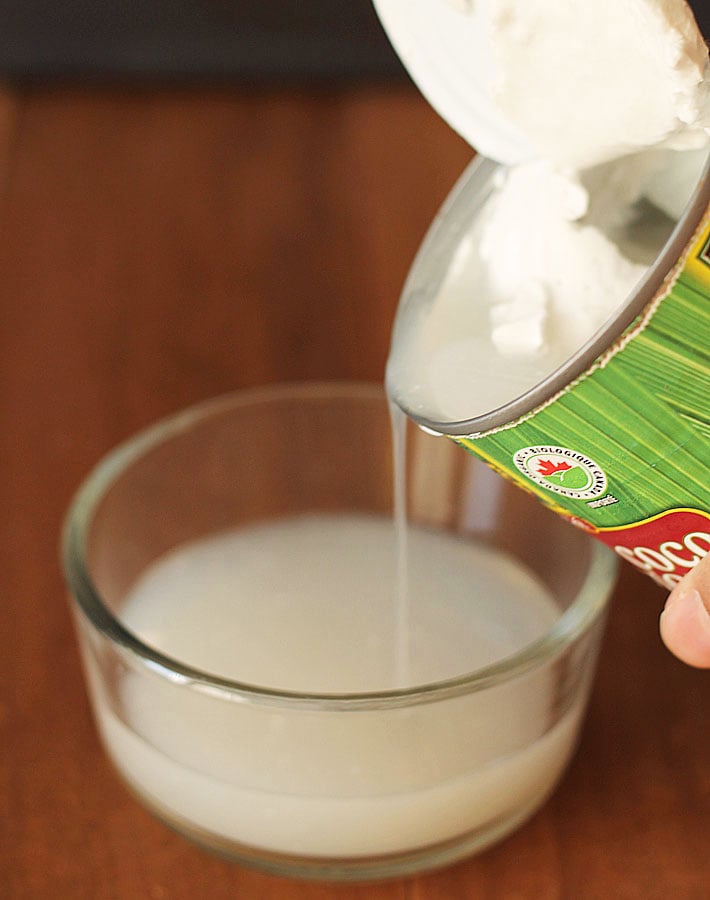 The liquid from a can of coconut milk being poured into a bowl.