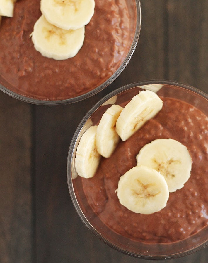 Overhead shot of two cups of Chocolate Banana Coconut Chia Pudding with sliced bananas on top.