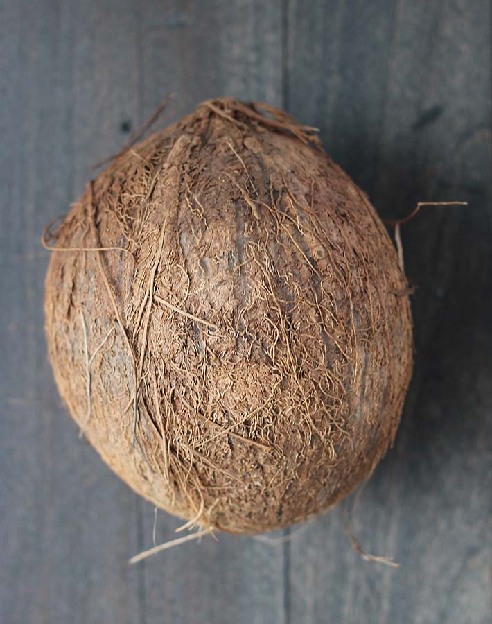 An overhead image of a fresh coconut on a dark wood table.