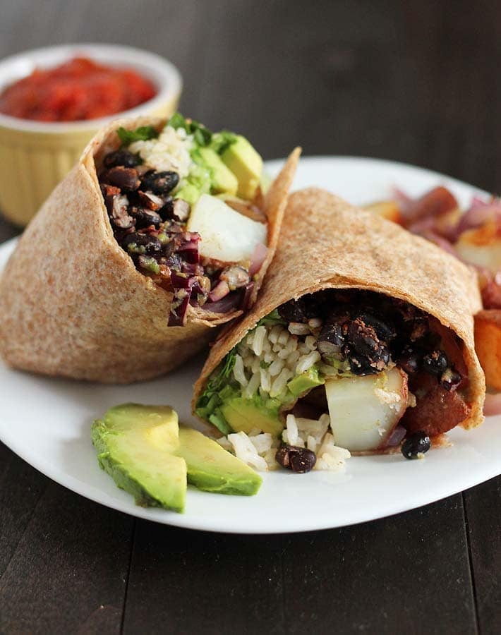 Vegan Breakfast Burrito on a white plate with avocado slices on the side of the plate.