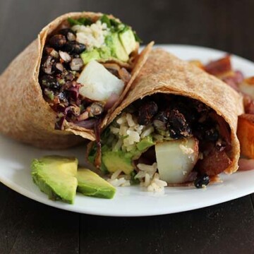 Vegan Breakfast Burrito on a small white plate, fried potatoes and avocado slices sit on the side of the burrito and a cup of salsa sits to the left of the plate.