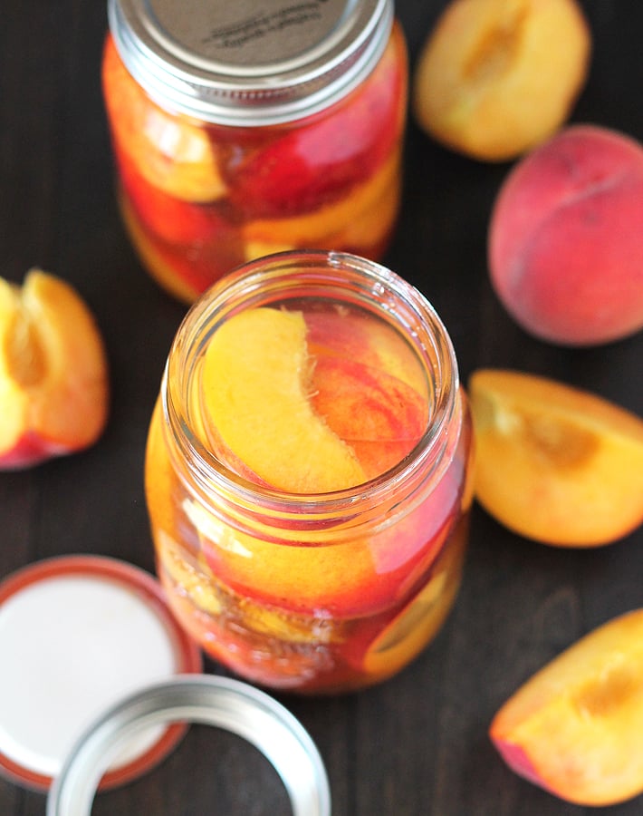 An overhead image of a glass jar filled with fresh peaches and liquid.