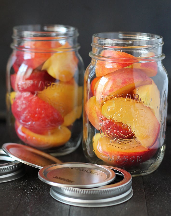 Two uncovered glass Mason jars filled with freshly sliced peaches.