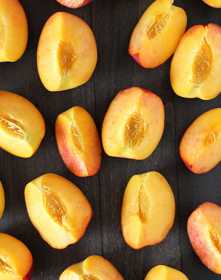 An overhead image showing sliced peaches on a dark wood table.