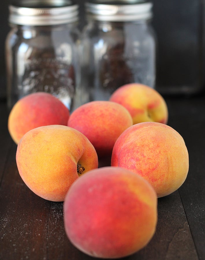 Fresh peaches on a table, two glass jars sit behind the peaches.