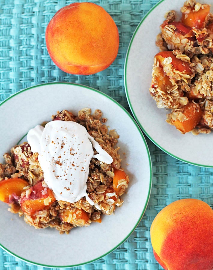 Overhead image of peach crisp on a plate, the peach crisp is garnished with whipped cream.