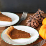 Two slices of pumpkin pie sitting on small white plates, forks are in front and to the sides of each plate.