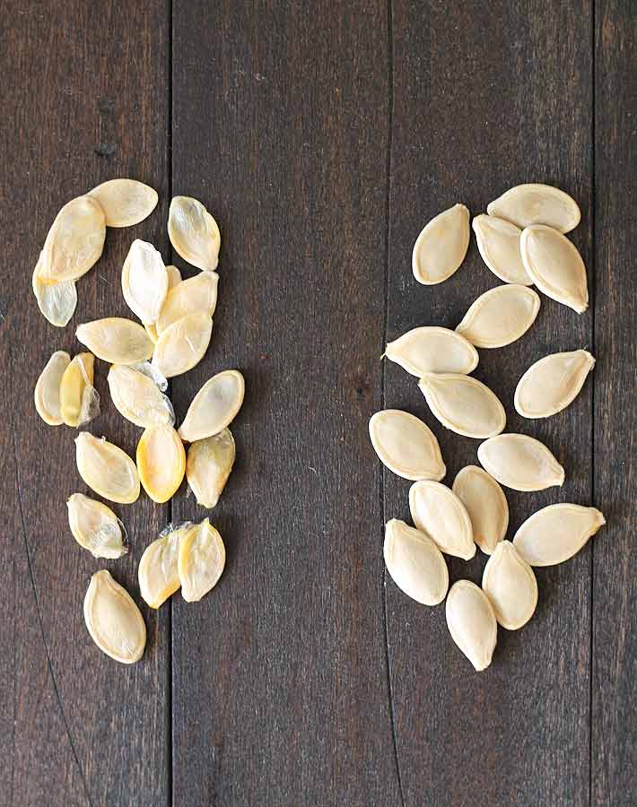 How to Roast Pumpkin Seeds - Pumpkin seeds on a dark wood table, seeds on the left are not suitable for roasting, seeds on the right are suitable.