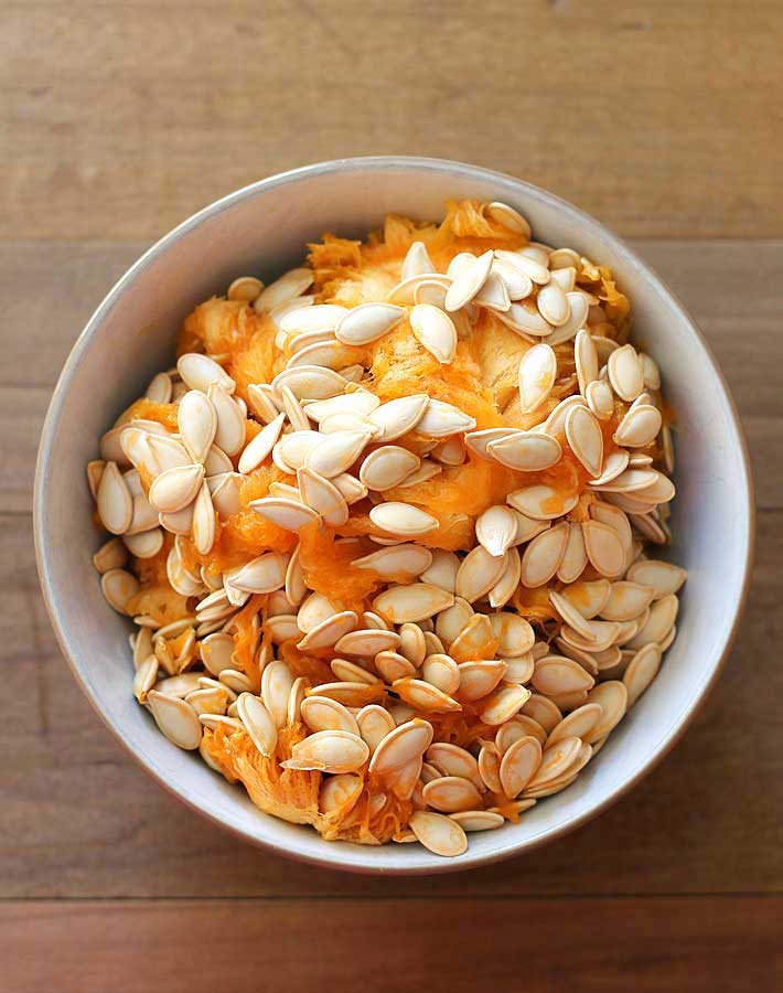 How to Roast Pumpkin Seeds - Pumpkin seeds scooped into a bowl, bowl is sitting on a brown wooden table.