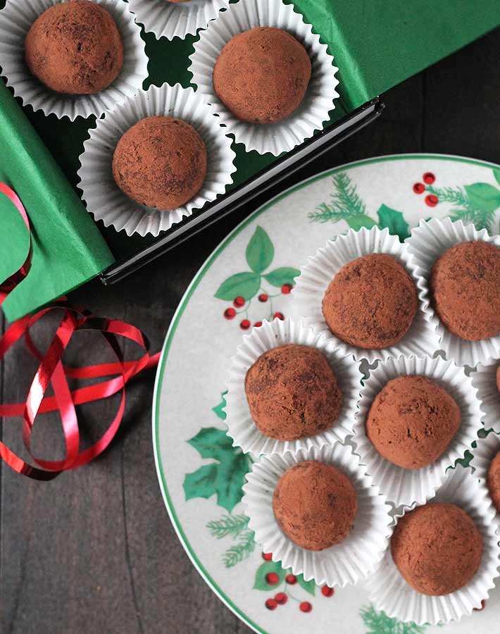 Overhead shot of eight Dark Chocolate Mint Truffles on a holiday plate, a box of truffles sits behind the plate.