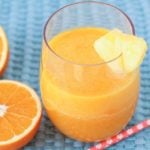 A glass of freshly-made Pineapple Orange Mango Juice on a blue placemat.