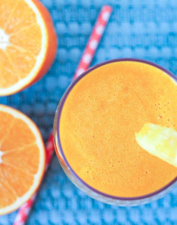 Overhead image of a glass of Pineapple Orange Mango Juice, a straw and two fresh orange pieces sit to the left of the glass.