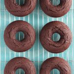 Six Vegan Gluten Free Baked Chocolate Doughnuts just out of the oven sitting on a wire cooling rack.