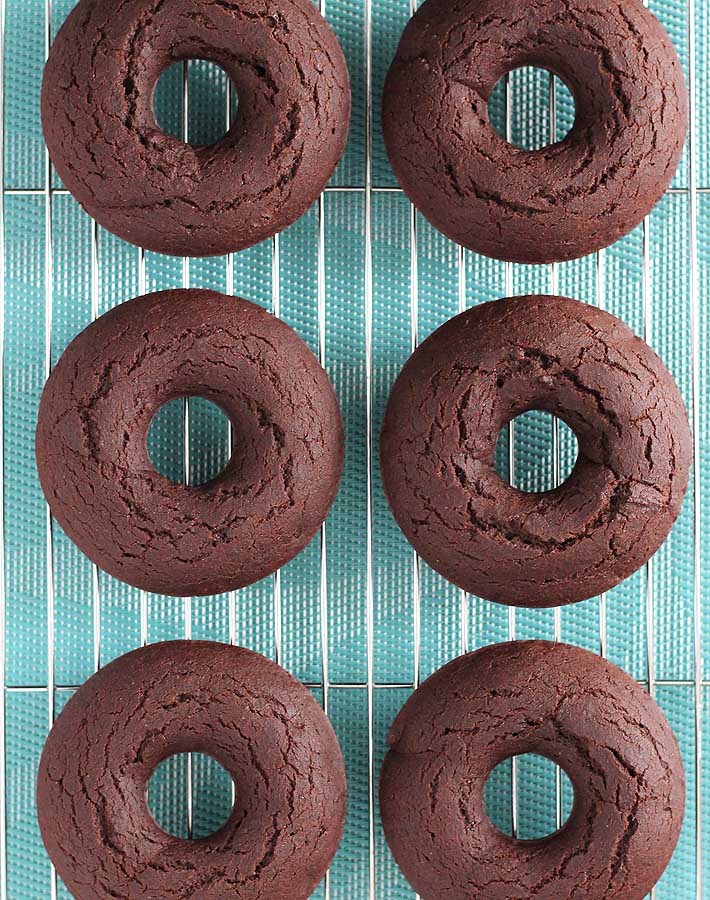 Six Vegan Gluten Free Baked Chocolate Doughnuts just out of the oven sitting on a wire cooling rack.