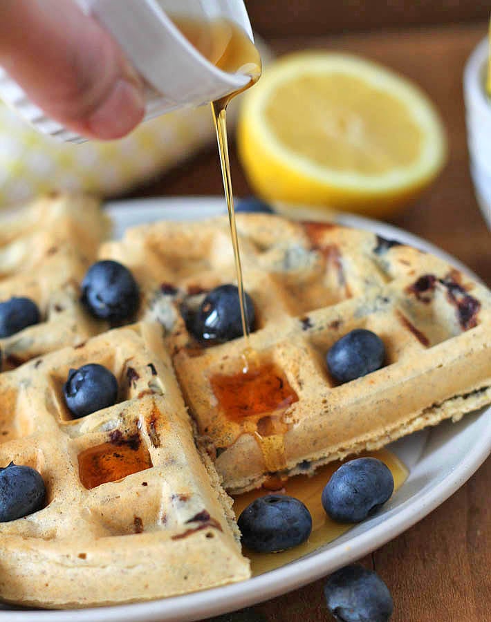 Maple syrup being poured onto Vegan Gluten Free Lemon Blueberry Waffles.