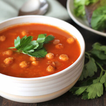 A bowl of soup with chickpeas garnished with fresh parsley.