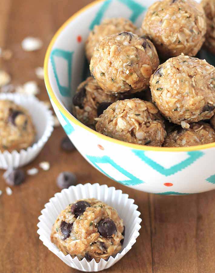 No Bake Peanut Butter Coconut Balls in a bowl and in mini muffin cups on a table.