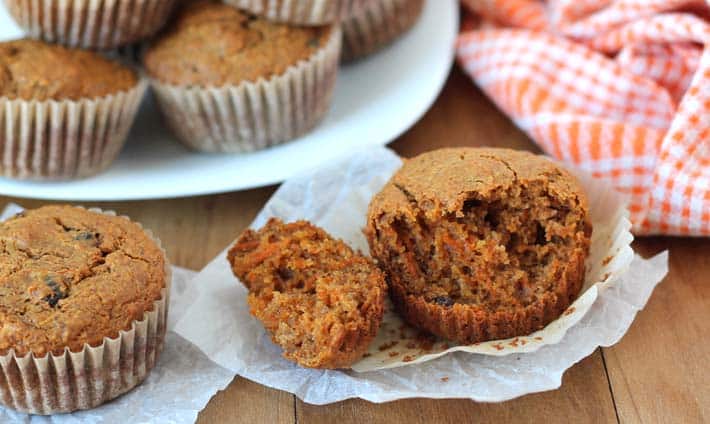 Carrot Ginger Muffins on a brown table, the muffin in the front has a chunk taken out of it.