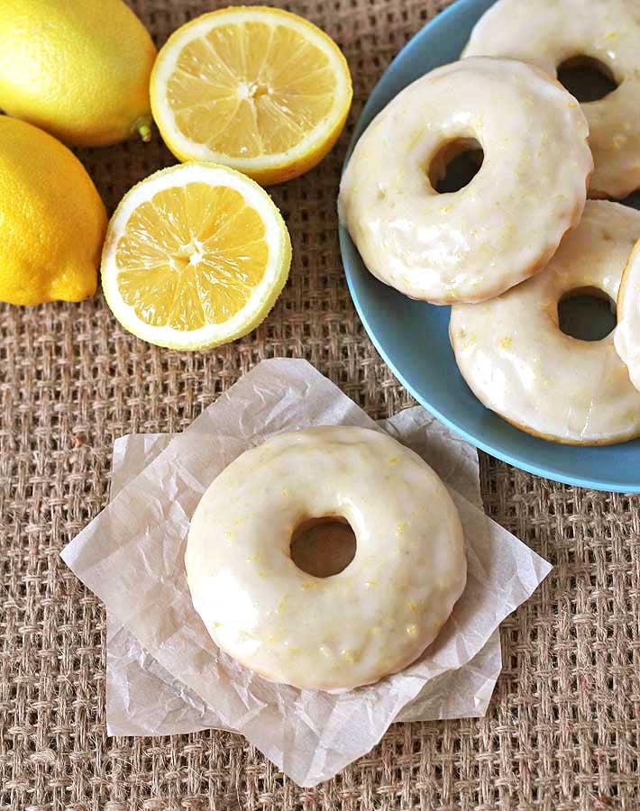 Overhead shot of Vegan Baked Lemon Doughnuts and fresh lemons on a burlap placemat.