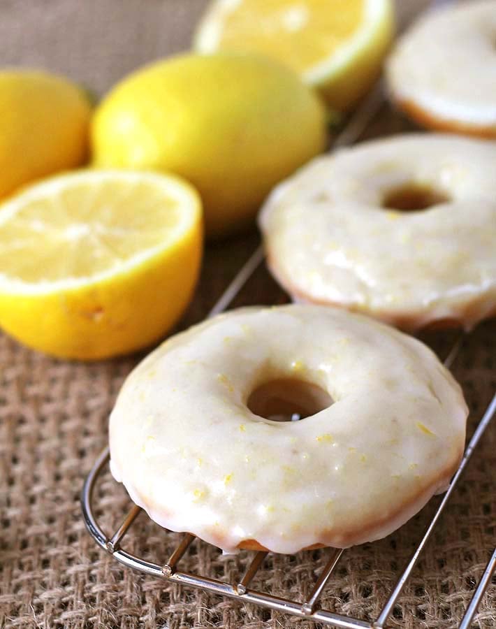 Vegan Baked Lemon Doughnuts sitting on a metal rack after being dipped in lemon glaze.