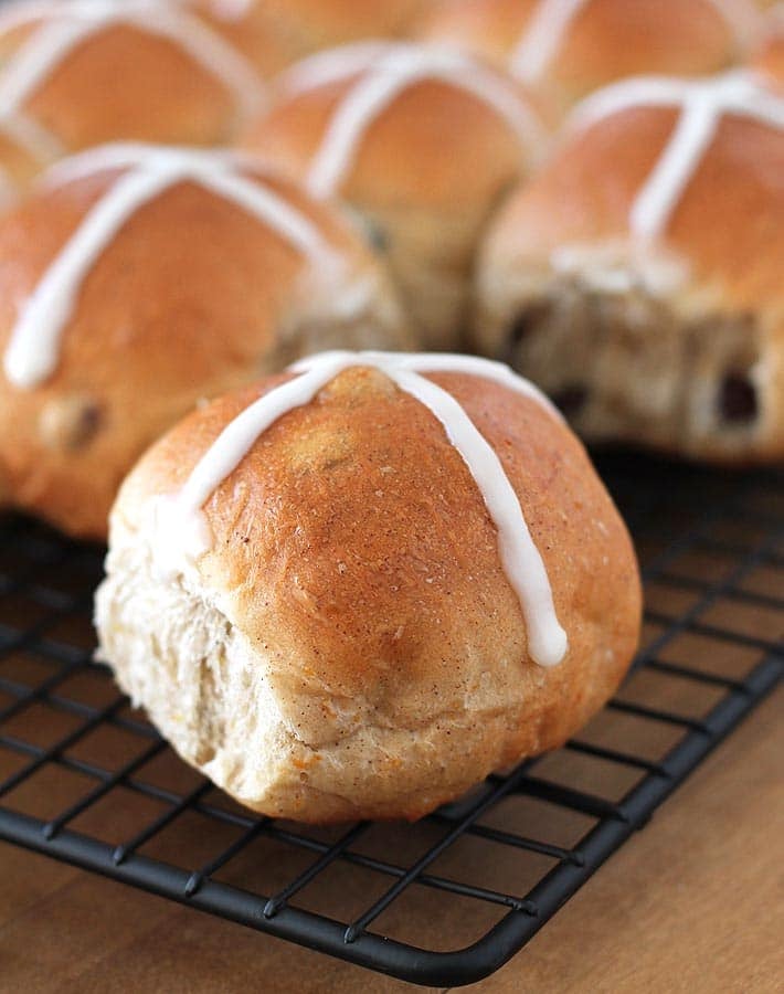 Vegan Hot Cross Buns just out of the oven on a black wire cooling rack.