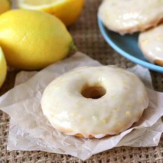 Vegan Baked Lemon Doughnuts on a blue plate int he background, one lemon doughnut sits in the foreground.