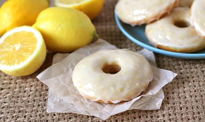 Vegan Baked Lemon Doughnuts on a blue plate int he background, one lemon doughnut sits in the foreground.