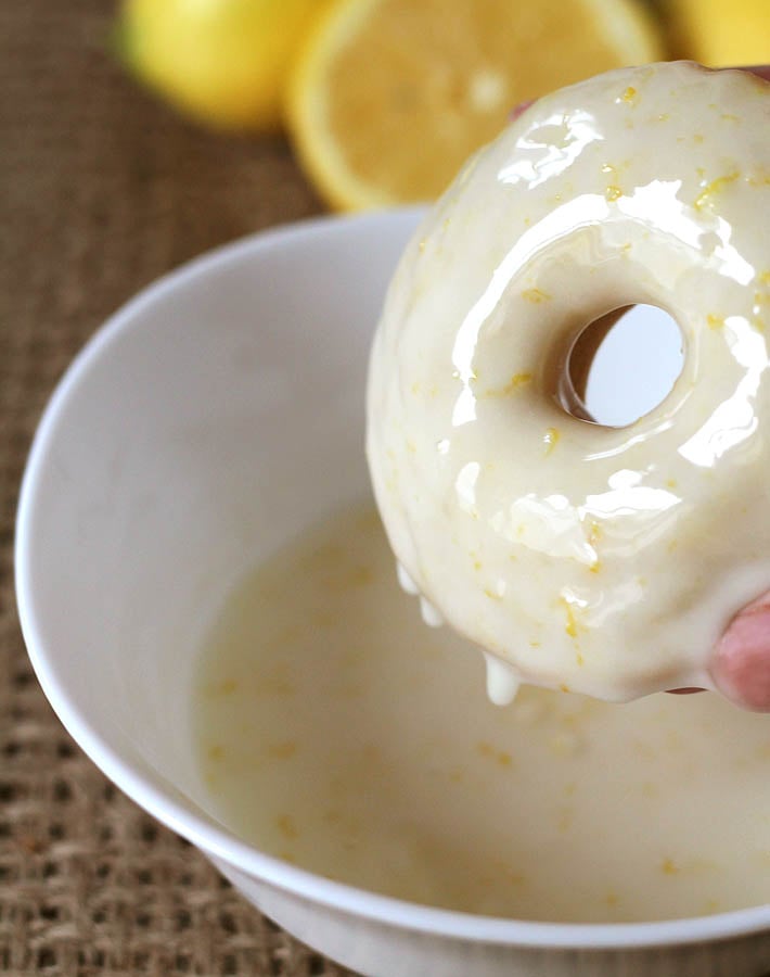 Vegan Baked Lemon Doughnuts being dipped into lemon glaze.