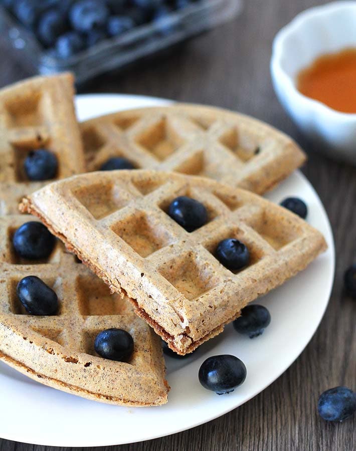 Easy Vegan Gluten Free Waffles on a white plate garnished with fresh blueberries, plate is sitting on a brown wood table.