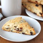 Coconut Raisin Vegan Scones fresh out of the oven and sitting on a plate with a mug of tea in the background.