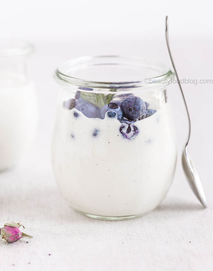 Cashew yogurt in a jar with blueberries on top and a spoon leaning on the side of the jar.