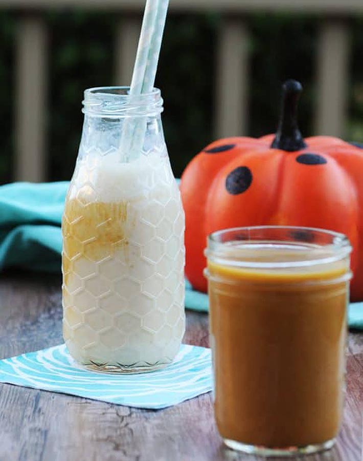 Vegan Pumpkin Spice Syrup in a jar with a pumpkin in the background.