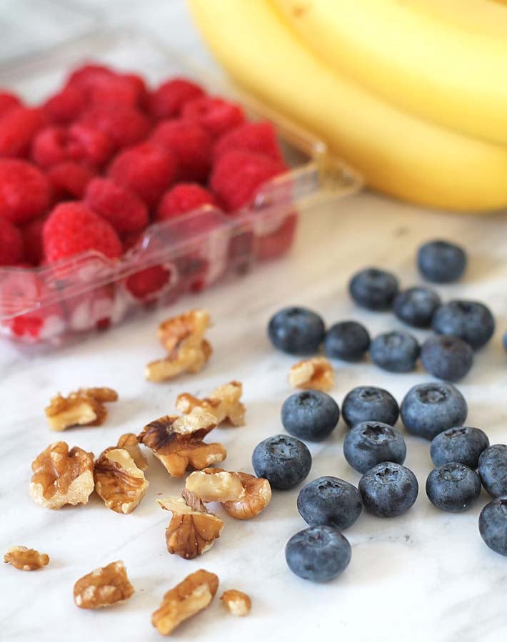 Bananas, raspberries, and blueberries all sitting on a marble surface, ingredients for a Berry Coconut Breakfast Bowl